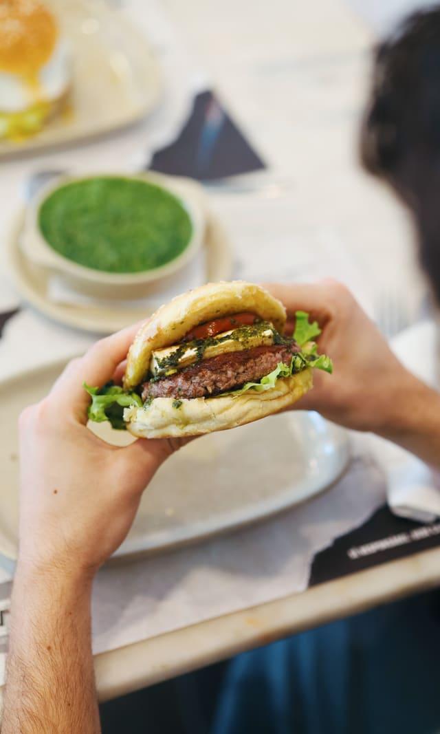 Burger held at the table with green sauce alongside