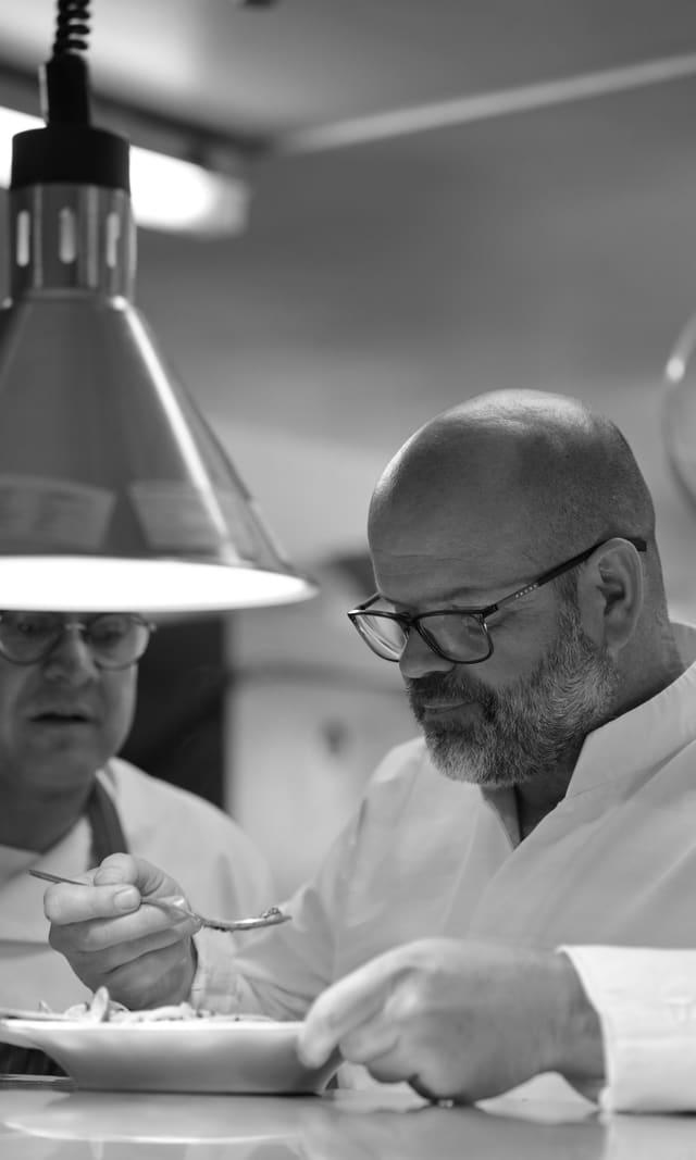Chef plating under the pass lamp, in black and white