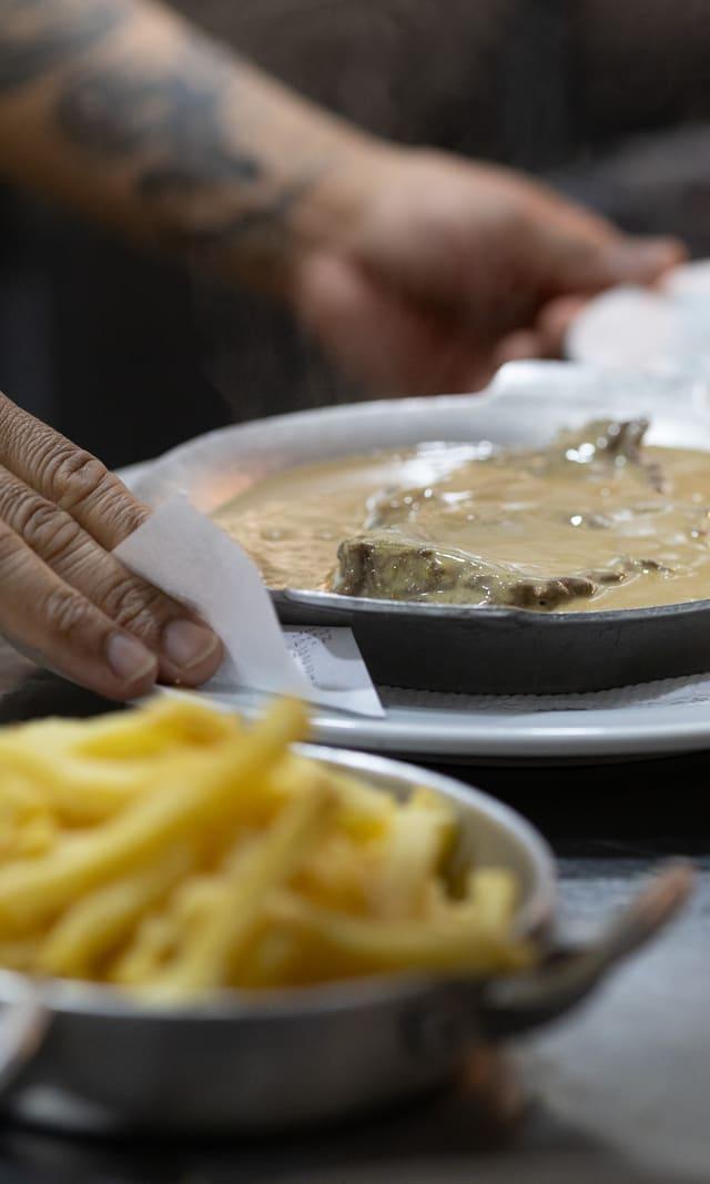 Hands serving pasta and a stew at a restaurant table